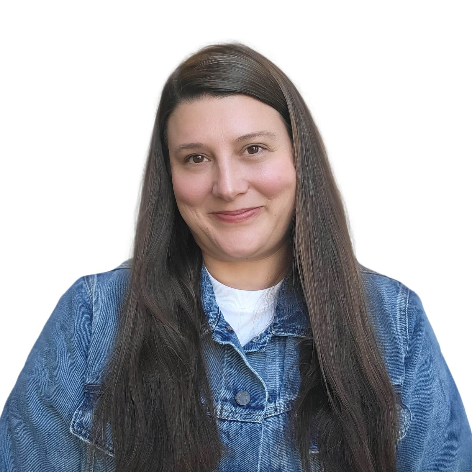 A person with long brown hair is wearing a denim jacket over a white shirt. They are smiling and have a plain white background behind them.