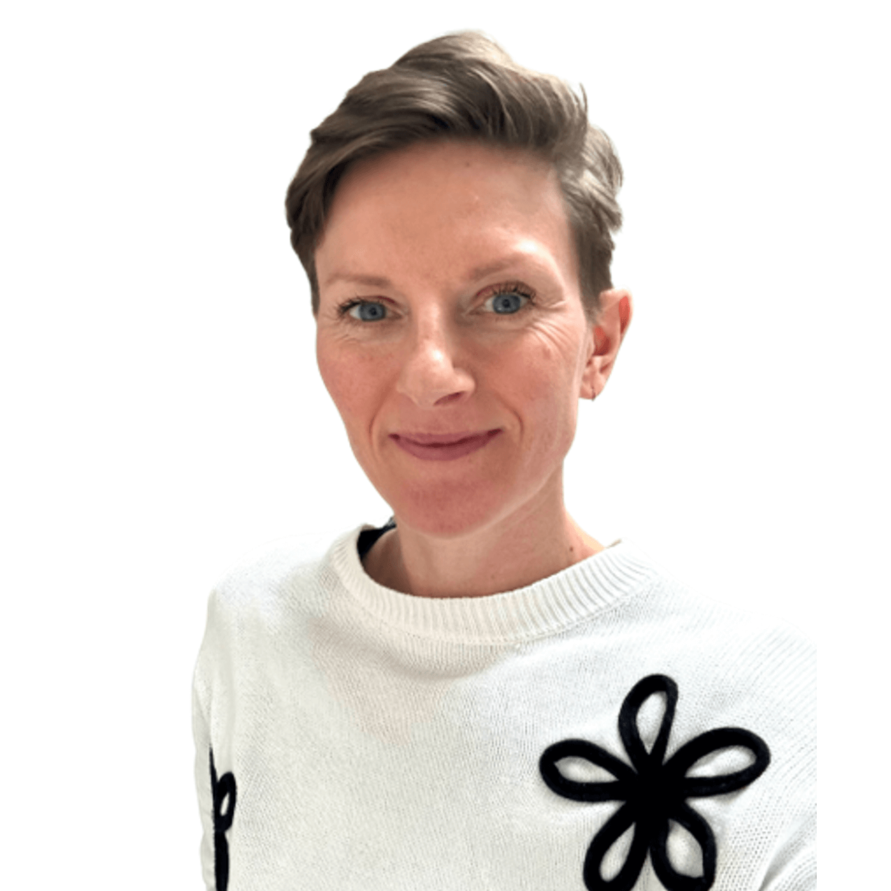 A woman wearing a white sweater adorned with black floral patterns, standing confidently against a neutral background.